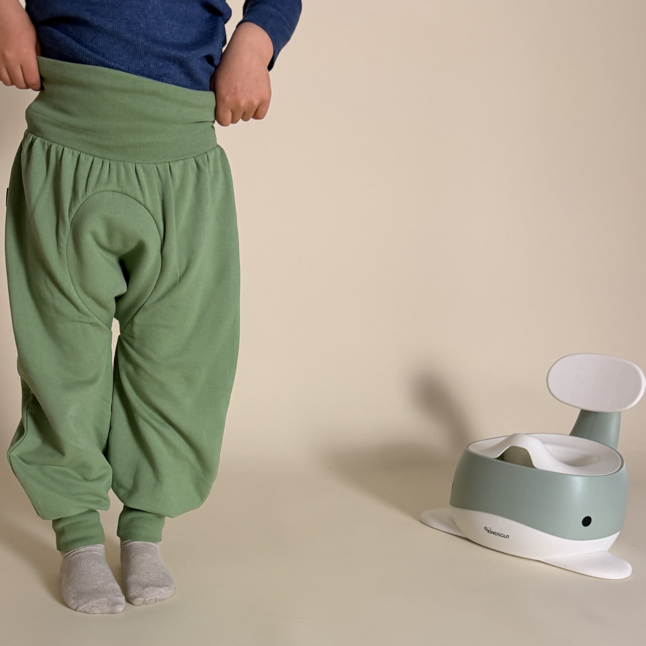 Windelfreikind zieht sich die Hose hoch, im hintergrund steht das Kindsgut Wal Töpfchen